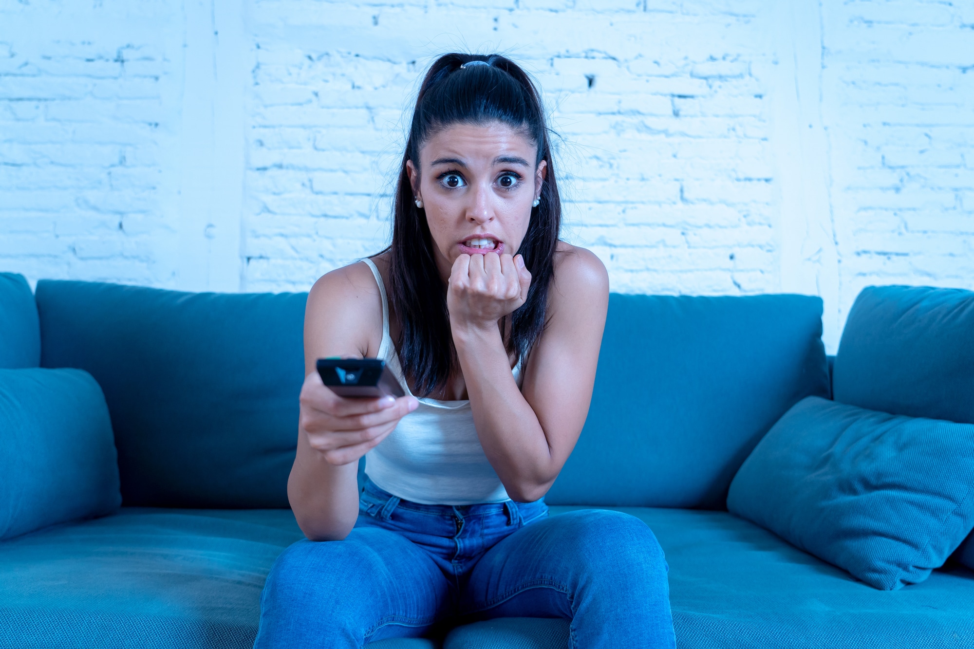 Young beautiful latin woman sitting at home sofa couch in living room watching horrible news